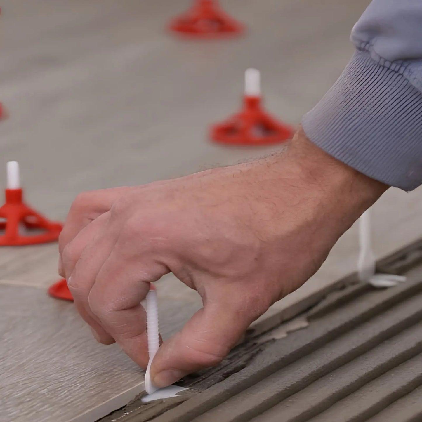 Anwendung eines Leveling Swiss Systems bei der Verlegung von grossen Bodenfliesen mit Fliesenkleber.